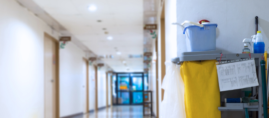 Long hospital hallway with cleaning cart and yellow trash bag.