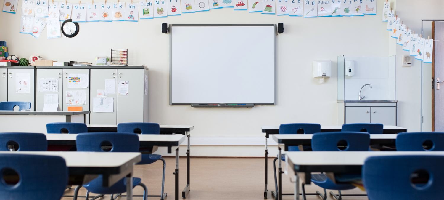 Empty classroom with blue chairs and a whiteboard on a light-colored wall.