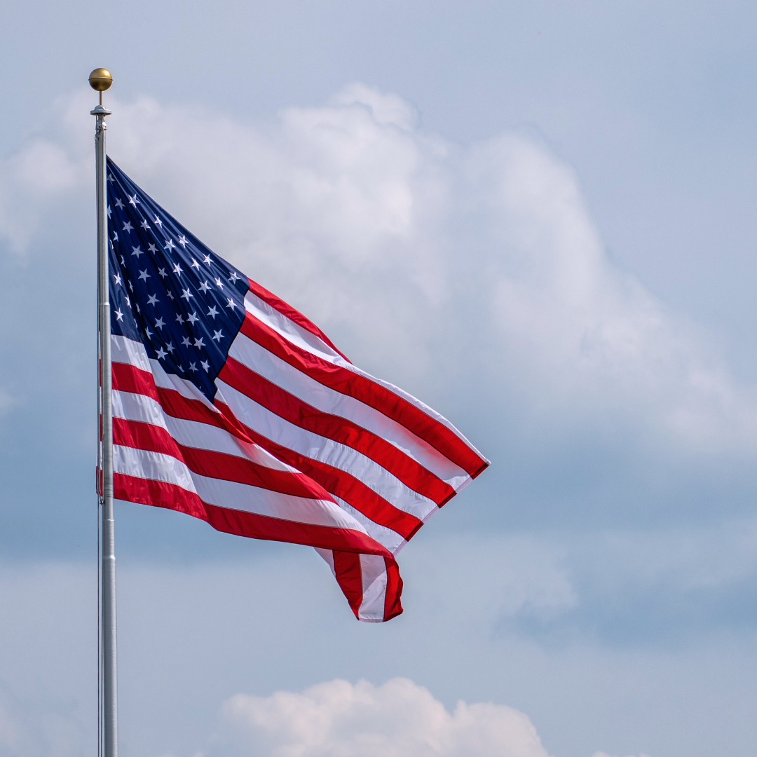 American flag waving against a blue sky with some clouds