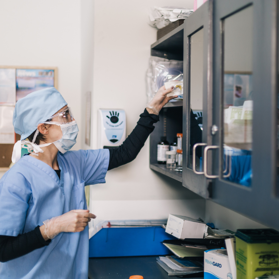 Person in medical scrubs reaching into a cabinet in a clinical setting