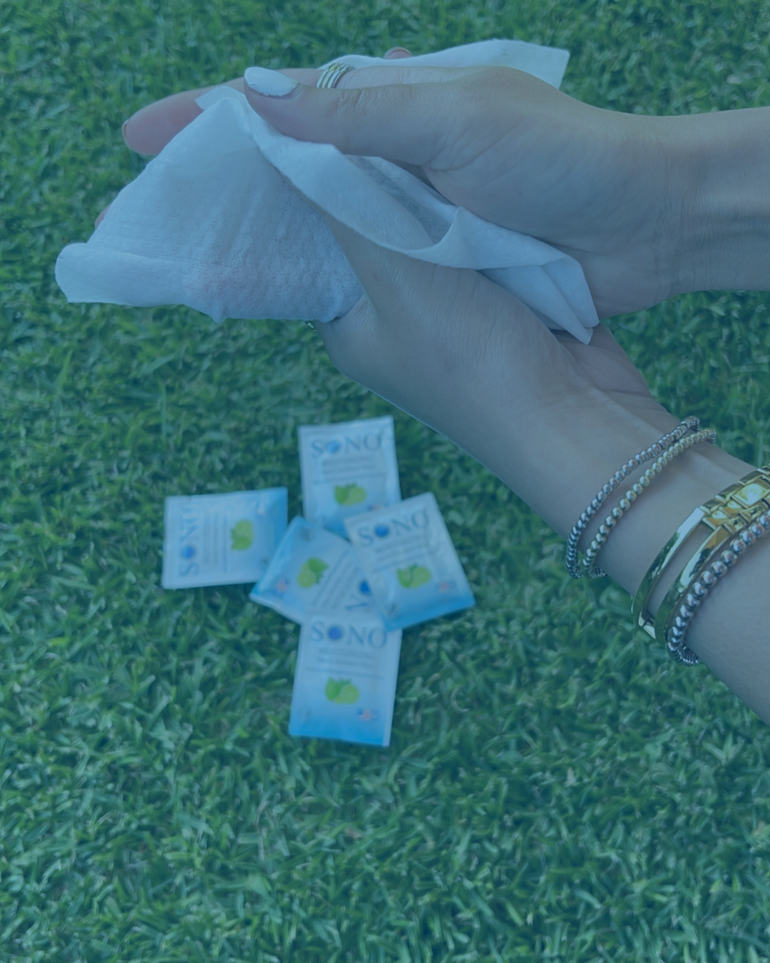 Hand holding a hand wipe with several similar packets on a grassy background