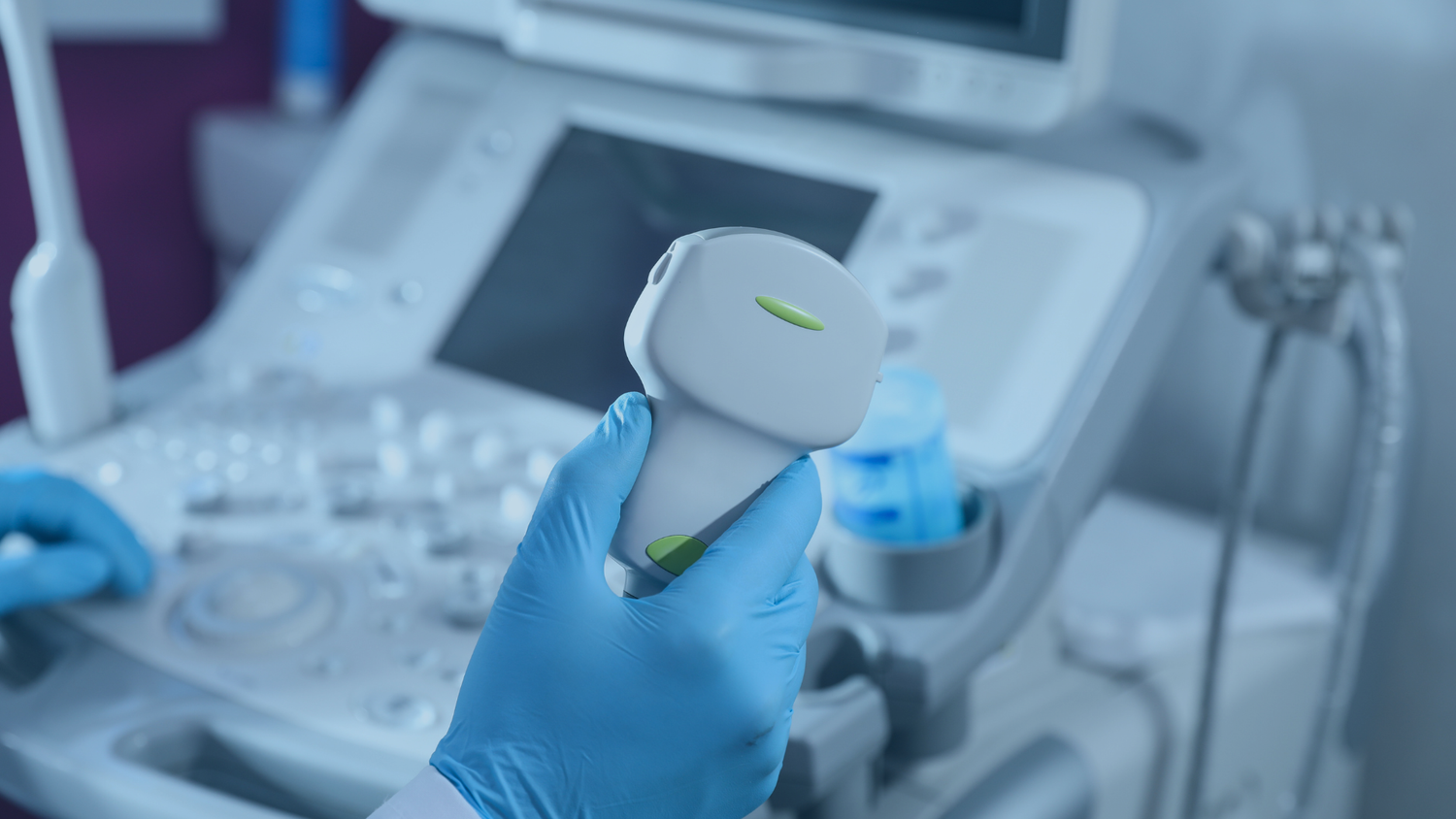 Person holding an ultrasound probe with medical equipment in the background