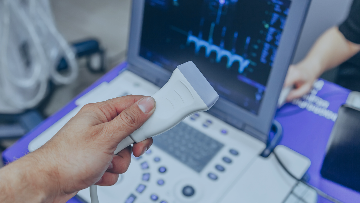 Hand holding an ultrasound transducer in front of a laptop on a medical table.